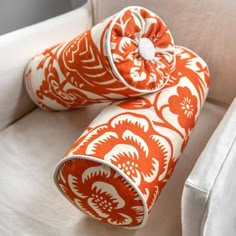 two orange and white pillows sitting on top of a white chair next to each other