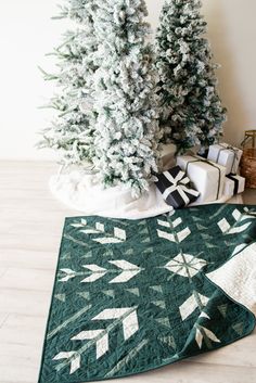 two christmas trees are on the floor next to a quilted table runner and gift bags