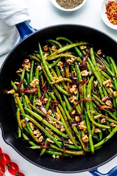 green beans with walnuts in a skillet next to tomatoes and seasoning on the side