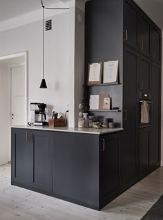 a kitchen area with black cabinets and counter top, coffee maker on the far wall