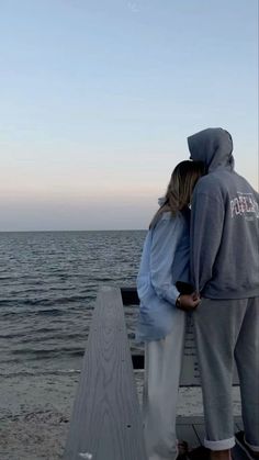 two people standing on a pier looking out at the water and one person is wearing a hoodie