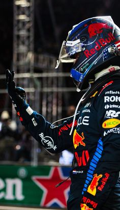 a man in a racing suit and helmet waves to the crowd while holding his hand out