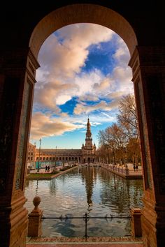 an arch leading to a large building with a clock tower in the distance and water running through it