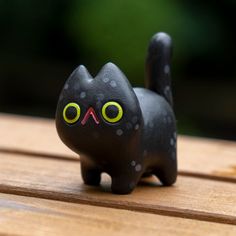 a black cat figurine sitting on top of a wooden table with green eyes