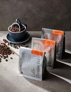 three bags of coffee sitting on top of a counter next to a cup and spoon