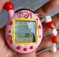 a hand holding a small pink and yellow electronic device with candy candies around it