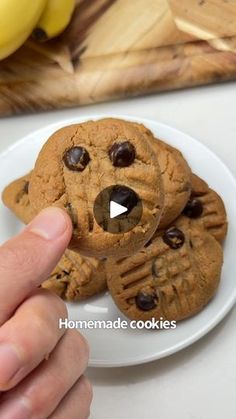 a person holding a cookie shaped like a dog on a plate with bananas in the background