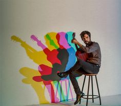 a man sitting on top of a stool next to a wall with a guitar painted on it