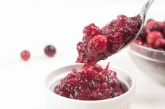 cranberry sauce being spooned into a bowl with cranberries in the background