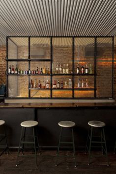 a bar with stools and shelves filled with bottles on the back wall, in front of brick walls