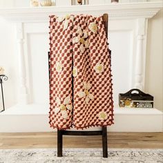 a red and white checkered curtain with flowers on it in front of a fireplace