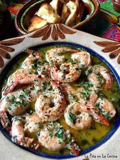 a plate with some shrimp and bread in it on a table next to other dishes