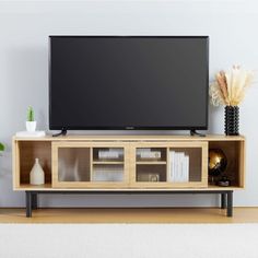 a flat screen tv sitting on top of a wooden entertainment center next to a vase