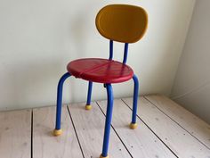 a red and blue chair sitting on top of a wooden floor next to a white wall