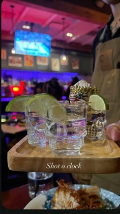 a person holding a tray with glasses and food on it in front of a bar