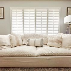 a white couch with pillows on top of it in front of a window covered by shutters