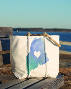 a white bag sitting on top of a wooden bench near the ocean with a heart painted on it