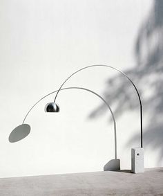 a lamp that is on top of a cement floor next to a white wall with a shadow