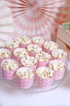 there are many cupcakes that are on the table with paper fans in the background