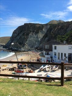 boats are parked on the beach in front of a house and cliff side area with people walking around