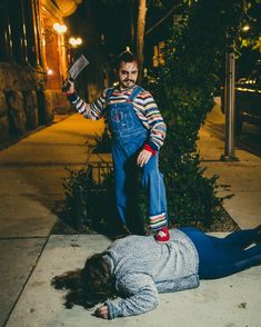 a man in overalls and clown makeup standing next to another person laying on the sidewalk