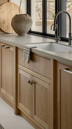 a kitchen sink sitting under a window next to a counter top with a vase on it