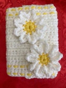 a white crocheted square with yellow and white flowers on the front, sitting on a red surface