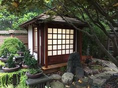 a small wooden building surrounded by trees and rocks in a garden with stones on the ground