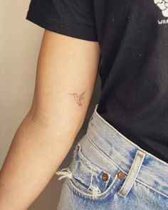 a person with a small bird tattoo on their left arm and the other arm behind them