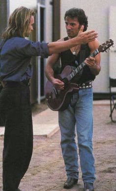 a man holding a guitar while standing next to a woman with her hands around him