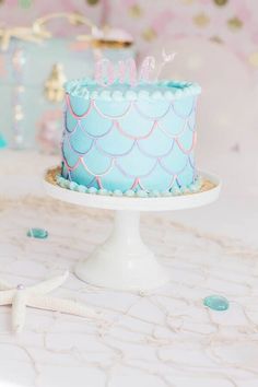 a blue cake with pink and white icing sitting on top of a table next to a starfish