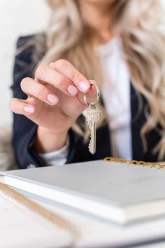 a woman holding a house key in her hand while sitting at a table with a book