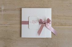 a wedding card with a pink ribbon and monogrammed initials on the front, sitting on a wooden surface