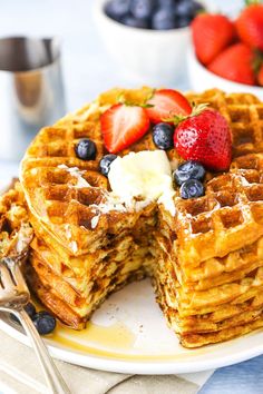 a stack of waffles with strawberries and blueberries on top, sitting on a plate