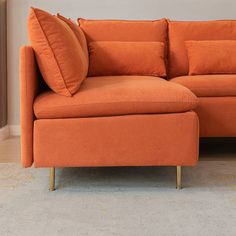 an orange couch with pillows on it in front of a white carpeted floor and wall