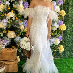 a woman standing in front of a flower wall wearing a white dress with ruffles