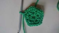 a crocheted green object is being worked on by a knitting needle and thread