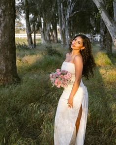 a woman in a white dress holding a bouquet of flowers and posing for the camera