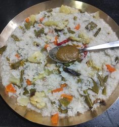 rice and vegetables are mixed together in a silver bowl with a spoon on the side