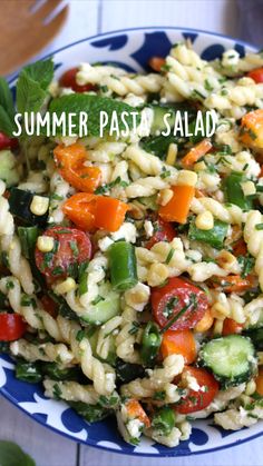 pasta salad with tomatoes, cucumbers and mint leaves in a blue and white bowl