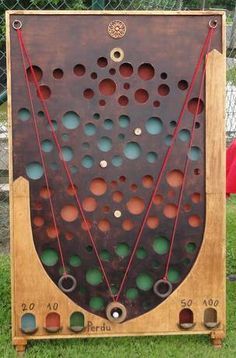 an old wooden board with holes and circles on it sitting in the grass next to a chain link fence