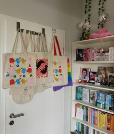 several bags hanging from hooks on the wall in front of bookshelves and shelves