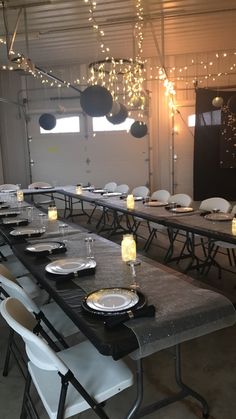 a long table with plates and silverware on it in a room that has lights hanging from the ceiling