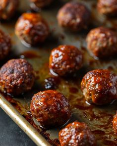 some meatballs are sitting on a baking sheet and drizzled with sauce