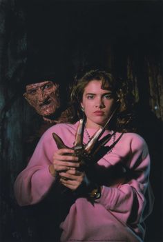 a woman holding two swords in front of a creepy man wearing a pink sweater and necklace