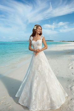 a woman standing on top of a beach next to the ocean wearing a wedding dress