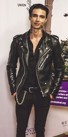 a man in black leather jacket standing on red carpet with his hands in his pockets