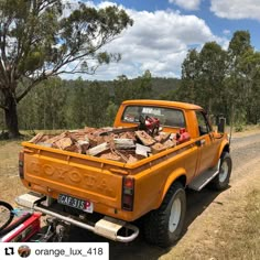 an orange pick up truck loaded with wood on the side of a dirt road next to trees