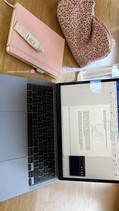 an open laptop computer sitting on top of a wooden table next to a pink purse