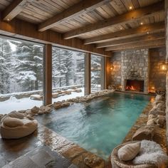 an indoor swimming pool surrounded by stone walls and flooring with large windows overlooking the snow covered trees